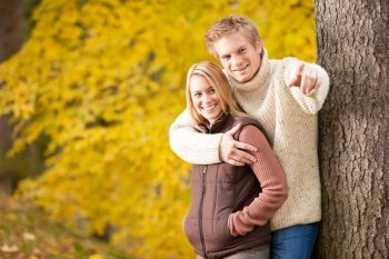 Autumn romantic couple happy together hugging in park tree pointing