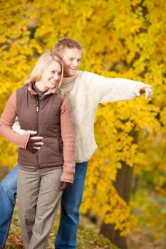 Autumn romantic couple happy together hugging in park pointing