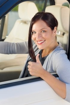 Attractive elegant businesswoman driving luxury new car thumb up smiling
