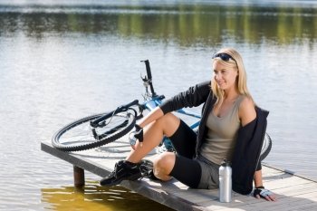Sport biking young woman sitting on pier by natural lake