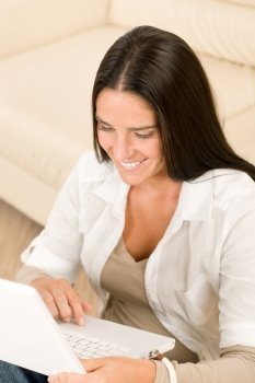 Attractive woman with laptop sitting by couch smiling