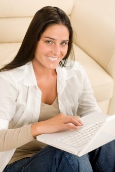 Attractive woman with laptop sitting by couch smiling