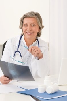 Doctor office - senior female physician hold x-ray sit behind desk