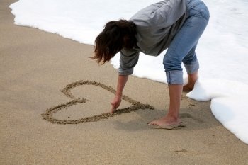 woman draws a heart in the sand on a beach