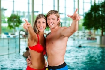Two young people - woman and man - at a public swimming pool standing in front of the water