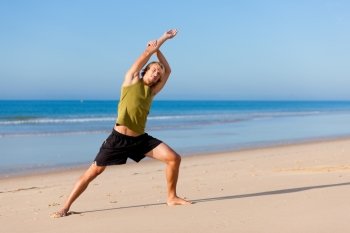 Young sportive man doing gymnastics on the beach
