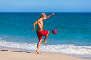 Young man on the beach playing soccer in his vacation