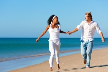 Happy couple - black woman and Caucasian man - walking and running down a beach in their vacation