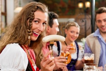 group of young men and women in traditional Bavarian Tracht having a breakfast with white veal sausage, pretzel, and beer