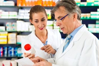 Two pharmacists with pharmaceuticals in hand consulting each other in a pharmacy