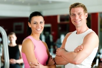 Sportive couple in gym or fitness club looking at the viewer