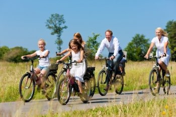 Family with baby and three girls having a weekend excursion on their bikes on a summer day in beautiful landscape