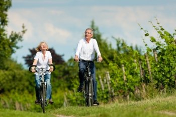 Happy mature couple - senior people, man and woman, already retired - cycling in summer in nature