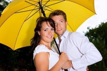 Happy couple in the summer rain with a yellow umbrella
