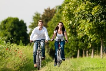 Happy young couple - man and woman - cycling in summer in nature