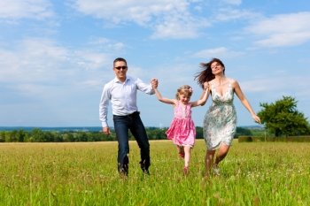 Happy family - mother, father, child - running over a green meadow in summer