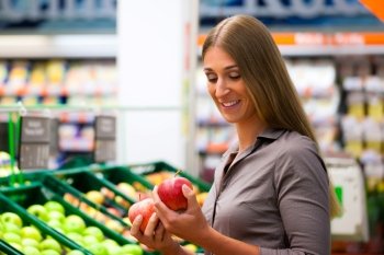 Woman in a supermarket at the shelf for fruits shopping for groceries, she is checking out the apples