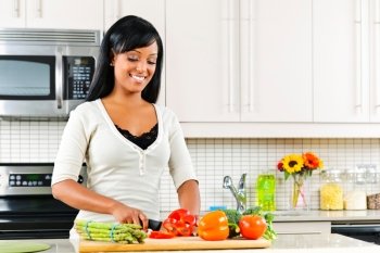 Smiling black woman cutting vegetables in modern kitchen interior