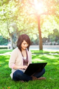 Mixed race college student sitting on the grass working on laptop at campus