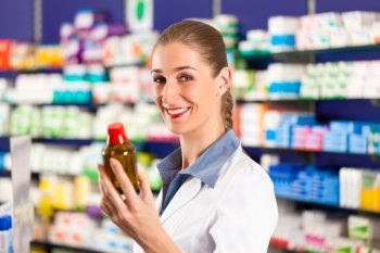 Female pharmacist is standing in her drugstore behind the counter and holds a medicine bottle