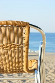 wicker chair stands on sandy beach