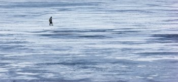 a lone fisherman is on the ice of winter river