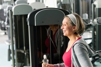 Senior woman relax at gym sitting by fitness machine