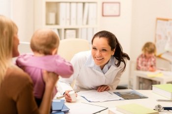 Female pediatrician smiling at baby patient sitting at office desk