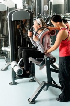 Fitness center senior woman exercise on machine with personal trainer