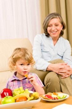 Little girl eat apricot fruit with grandmother relaxing on sofa