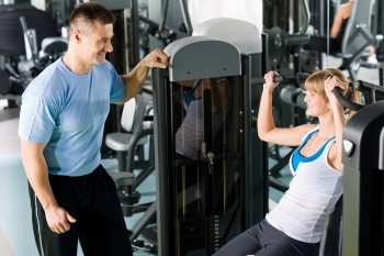 Young woman exercise on shoulder press machine with personal trainer