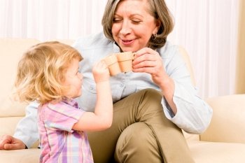 Grandmother with little girl drink tiny cups toasting happy home