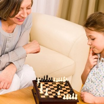 Young girl playing chess with grandmother together at home