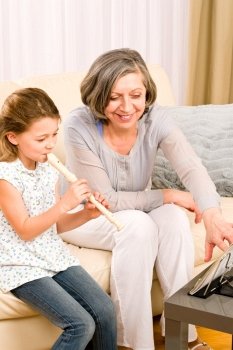 Grandmother teach young girl to play flute happy sitting on sofa