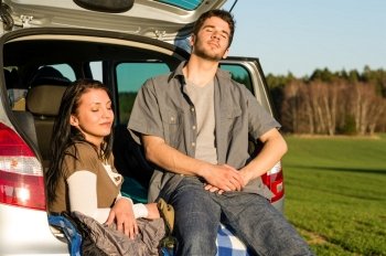 Happy camping couple lying inside car enjoy summer sunset countryside