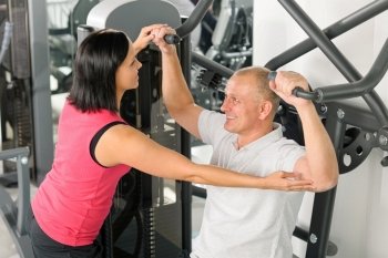 Fitness center personal trainer assist man exercise shoulder on machine