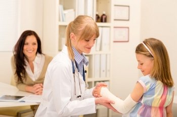 Female pediatrician checking bandage of girl broken arm