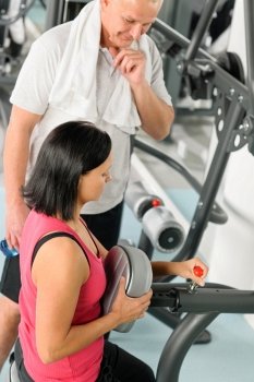 Active man watch personal instructor adjust machine level at gym