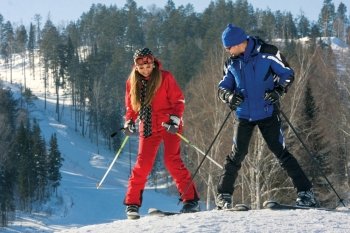 A beautiful young woman on ski along with a handsome instructor against a snowfield.