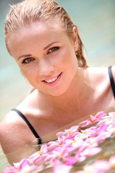 Beautiful woman bathing in pool with frangipani flowers