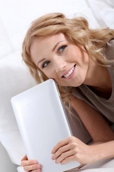 Smiling blond woman at home using electronic tablet