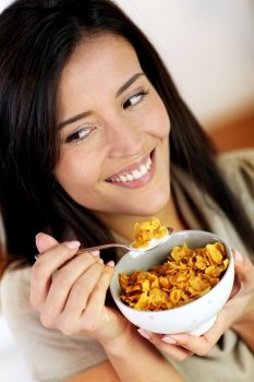 Cheerful woman eating corn flakes for breakfast