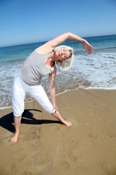 Senior woman doing stretching exercises on the beach