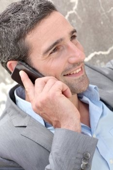 Businessman talking on mobile phone against wall