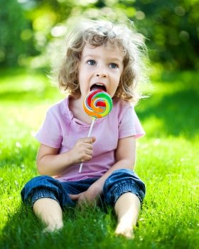 Happy child eating lollipop on green grass outdoors in spring park