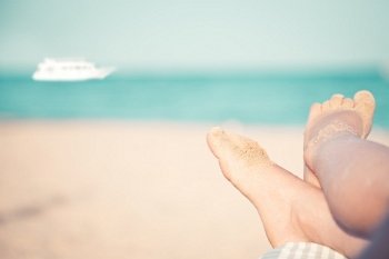 Children`s feet at the beach against sea and ship. Summer vacations concept