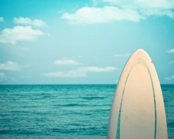 Old grunge surfboard against calm sea. Retro toned image