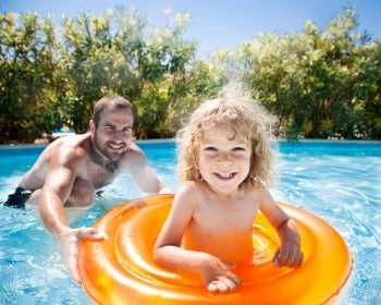 Happy child playing with father in blue water of swimming pool on a tropical resort at the sea. Summer vacations concept