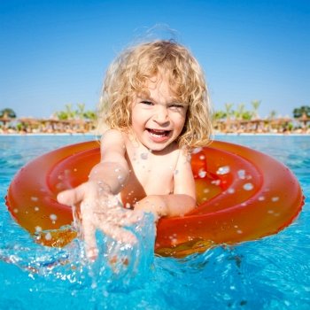Happy child playing in blue water of swimming pool on a tropical resort at the sea. Summer vacations concept