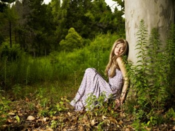 A beautiful young lady sitting in a tree in the forest